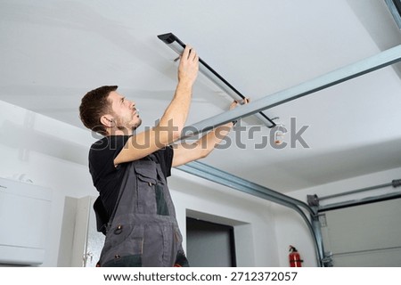 Man in workwear installing a linear LED light fixture on the ceiling indoors. Concept of electrical installation, maintenance work and home renovation.