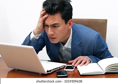 Man With Worried And Confused Look Holding Hear While Looking At The Laptop