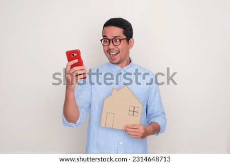 A man with wow expression looking to mobile phone and holding house shape cardboard