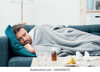 Man wrapped in plaid lying on the sofa feeling sick illness at home - Shutterstock ID 1664185675