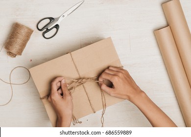 Man Wrapping Gift. A Parcel Wrapped In Brown Paper And Tied With Rough Twine