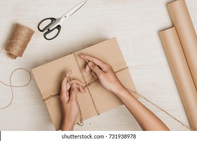 Man Wrapping Gift. A Parcel Wrapped In Brown Paper And Tied With Rough Twine