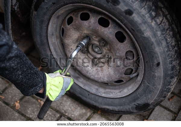 A man with wrench screw car wheel nut. Green dirty\
gloves in his hands.
