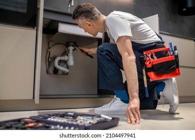 Man with wrench touching pipe under sink - Powered by Shutterstock