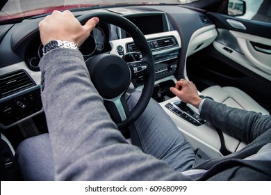 Man with wristwatch driving a luxury car, holding hand on steering wheel and gearbox knob - Powered by Shutterstock