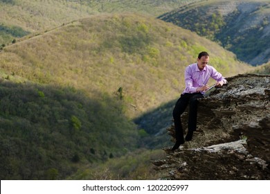 man writes in notepad sitting on stone