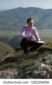 man writes in notepad sitting on mountain