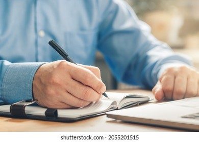 Man writes notes in his diary and planning new business goals at the table in the office, hand with a pen, close-up view.