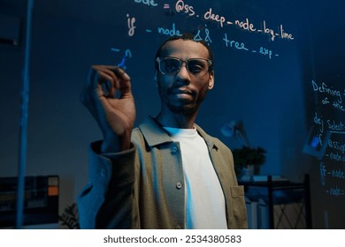 Man Writing Code on Transparent Board in Dimly Lit Room