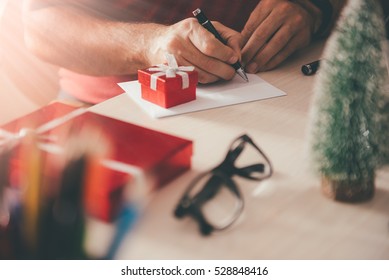 Man Writing Greeting Card On Table Beside Small Red Gift Box