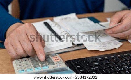 A man is writing a household ledger while organizing receipts. A close-up of hands. Tax or year-end settlement concept.
