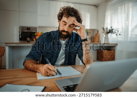 Man writing in notebook while feeling stressed and overwhelmed by work from home