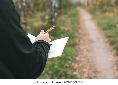 A man is writing in a notebook while standing in a forest. Concept of solitude and introspection, as the man is alone in the woods, surrounded by nature