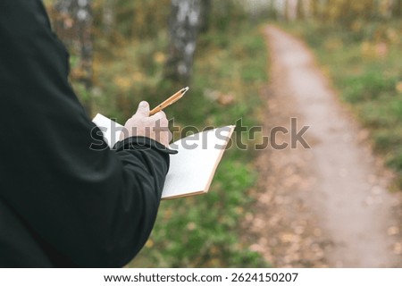 A man is writing in a notebook while standing in a forest. Concept of solitude and introspection, as the man is alone in the woods, surrounded by nature