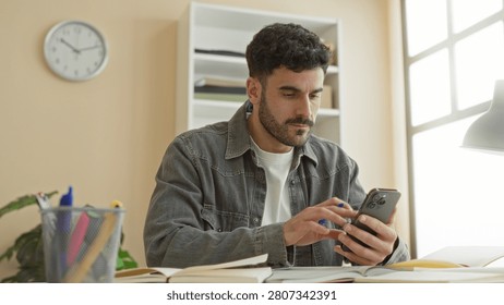 Man writing notes in a notebook with smartphone in hand at a study desk in a building; concentration productivity.