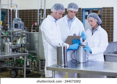 Man writing on clipboard while colleagues testing product in the factory