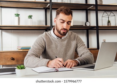 Man writing on notebook beside laptop on table - Shutterstock ID 1579966777