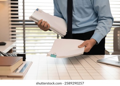 A man is writing on a stack of papers with a pen. The papers are organized in a neat stack on a table. The man is focused on his work, possibly preparing a report or a document
