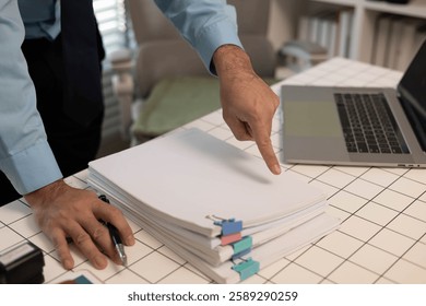 A man is writing on a stack of papers with a pen. The papers are organized in a neat stack on a table. The man is focused on his work, possibly preparing a report or a document
