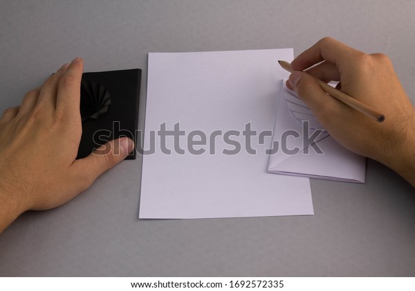 Man writing on white sheet with black\
and white letter envelopes on silver\
background
