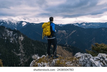 A man with a yellow backpack on a hill. View of snowy mountains. Sportswear, tourist photo for travelers. Adventure in nature. - Powered by Shutterstock