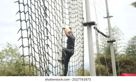 man in yellow helmet climbs a high net during an obstacle course - Powered by Shutterstock