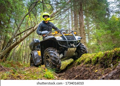 A man in a yellow helmet rides a Quad bike through the woods. Quad bike on a forest road. Journey through the forest on a Quad bike. Sale and rental of ATVs. Driving on bad roads.