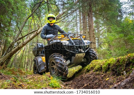 A man in a yellow helmet rides a Quad bike through the woods. Quad bike on a forest road. Journey through the forest on a Quad bike. Sale and rental of ATVs. Driving on bad roads.
