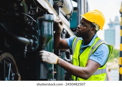 A man in a yellow helmet and safety vest is working on a train engine. He is wearing gloves and he is focused on his task - Powered by Shutterstock