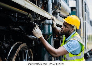 A man in a yellow helmet and safety vest is working on a train engine - Powered by Shutterstock