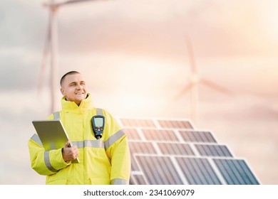 a man in a yellow jacket holding a tablet.  Sustainable Energy Engineer. A Technician's Work on Solar Panels and Wind Turbine Farm. - Powered by Shutterstock