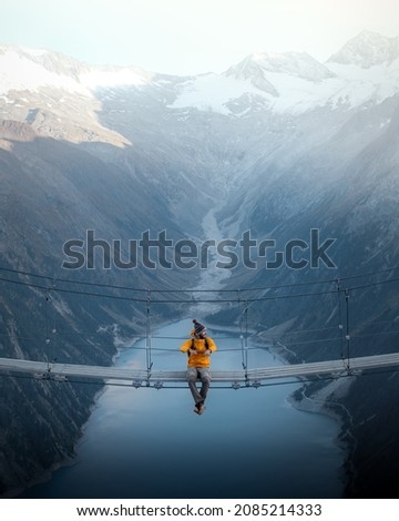 
Man in yellow jacket sitting on a suspension bridge over a lake in Olpererhutte, Austria