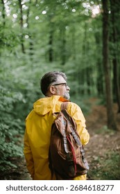 Man in a yellow rain jacket and backpack walking on a forest trail, enjoying the outdoors and nature