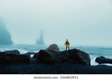 A man in a yellow raincoat is enjoying wild nature in Iceland. An explorer is watching waves on the seacoast and enjoying wild nature and stormy weather on the coast of Iceland.