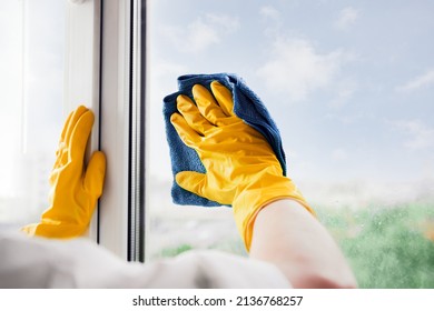 Man in yellow rubber gloves cleaning window glass with cleaner spray detergent and squeegee or rag at home, office, copy space. Housework and housekeeping, home hygiene. Blue sky view, plastic windo