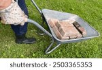 A man with a yellow shirt and blue trousers drives a wheelbarrow with bricks.