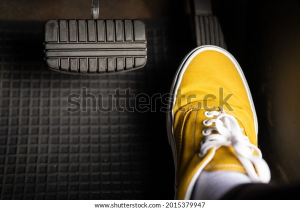 A man in yellow sneakers is stepping on the\
accelerator of a car.