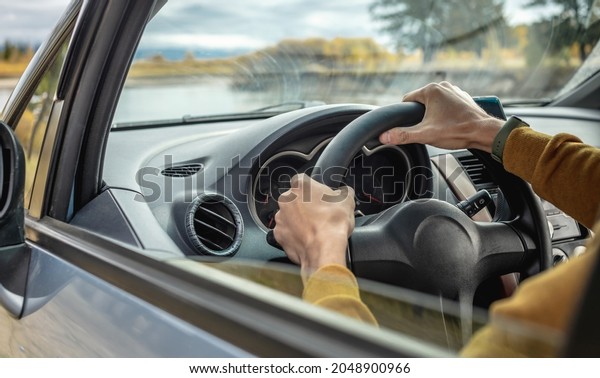 Man in yellow sweater is driving a car along the\
river and the beautiful autumn forest. Concept of nature, travel\
and autumn mood. Closeup