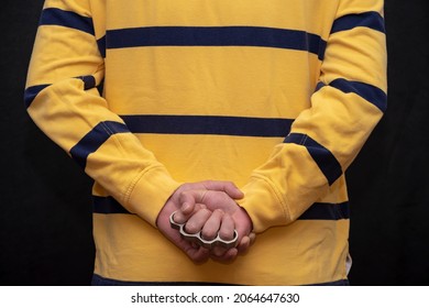 A Man In A Yellow Sweater Is Holding A Metal Brass Knuckle Behind His Back, Preparing For A Fight, The Average Plan.  Concept: Serious Injury, Street Gangs, Crime In The City.