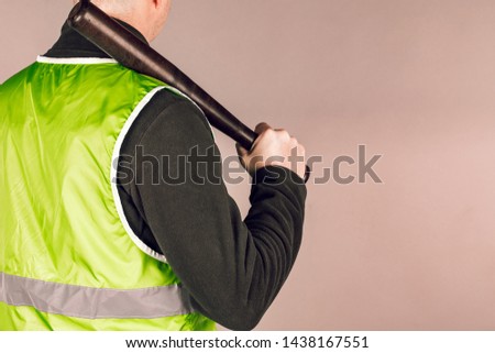 man in a yellow vest, a Builder or a protester with a baseball bat in his hands on a gray background.