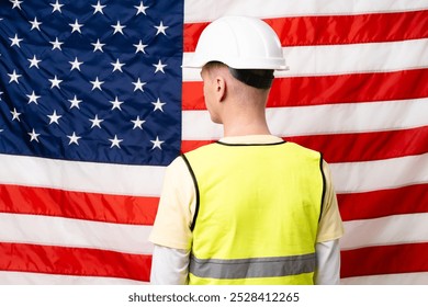 Man in a yellow vest stands in front of an American flag. He is wearing a hard hat - Powered by Shutterstock