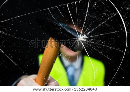 A man in a yellow vest and suit smashes glass with a hammer, the concept of riots and protests in France