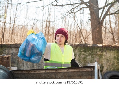 Man In Yellow Vest Throws Blue Trash Bag Out In The Dumpster