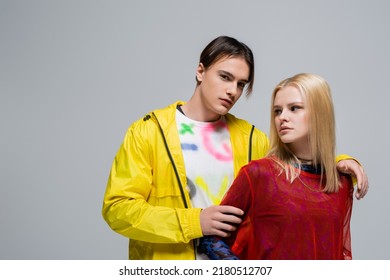 Man In Yellow Windbreaker Hugging Girlfriend And Looking At Camera Isolated On Grey