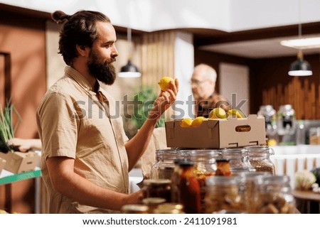 Man in zero waste store taking time to analyze fruits, making sure they are handpicked and farm grown. Green living customer thoroughly checking local supermarket food items are ethically sourced