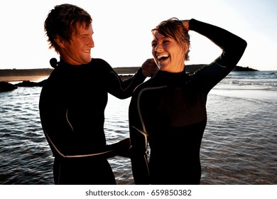 Man Zipping Up Laughing Woman's Wetsuit