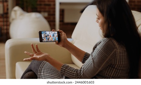 Management executive using smartphone to delegate project tasks to employees during videoconference meeting. Manager at home holding internet videocall on phone with diverse team