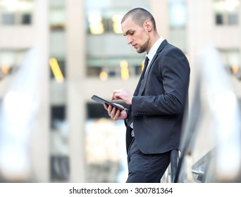 Manager. Businessman Working For Digital Tablet On The Background Office Center Building. Working Out Of The Office. Young Arab Business Man Writing Something In His Note Pad And At Not Looking Camera