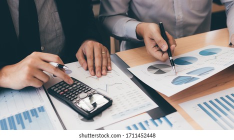 Manager calculates about the company finances by pressing on the calculator on the table with the employee explaining the summary report of the company cost at the office.