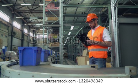 Manager checking delivery and inventory. Man standing near packaging line writing some information. Handsome professional worker wearing white shirt and jeans working in warehouse.